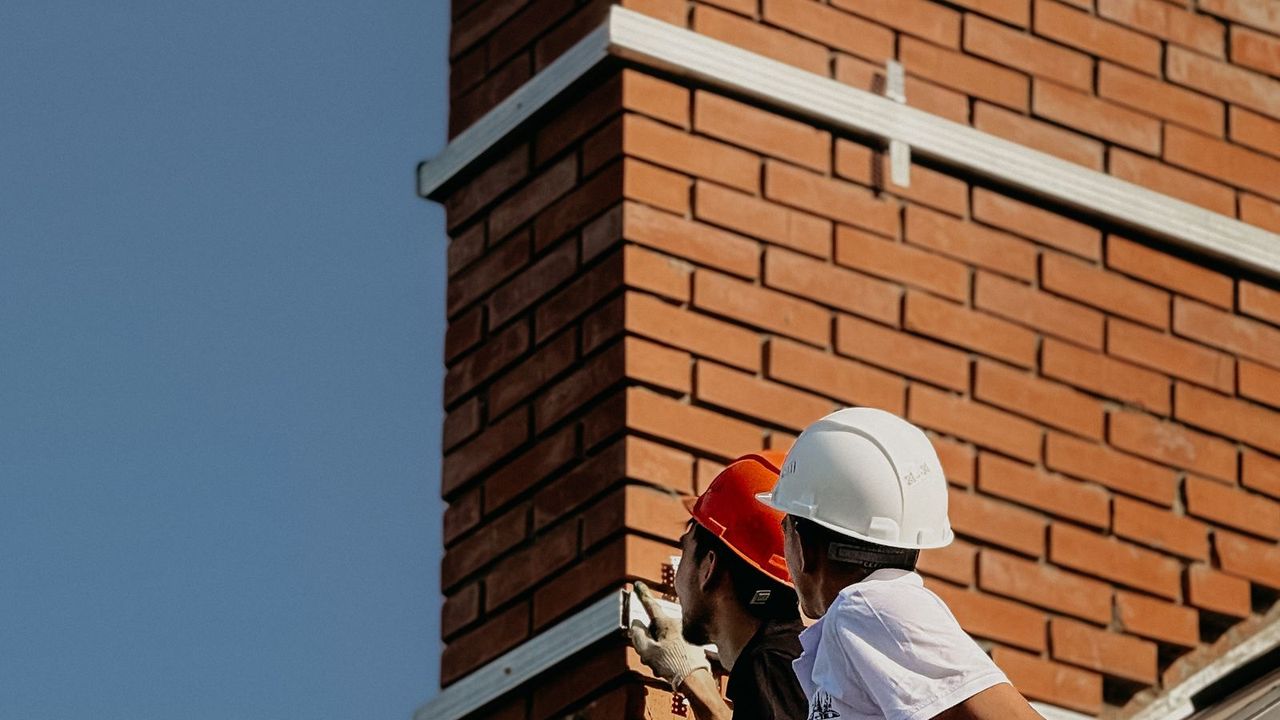 Couvreurs reprenant le solin d'une souche de cheminée, cause fréquente d'infiltration